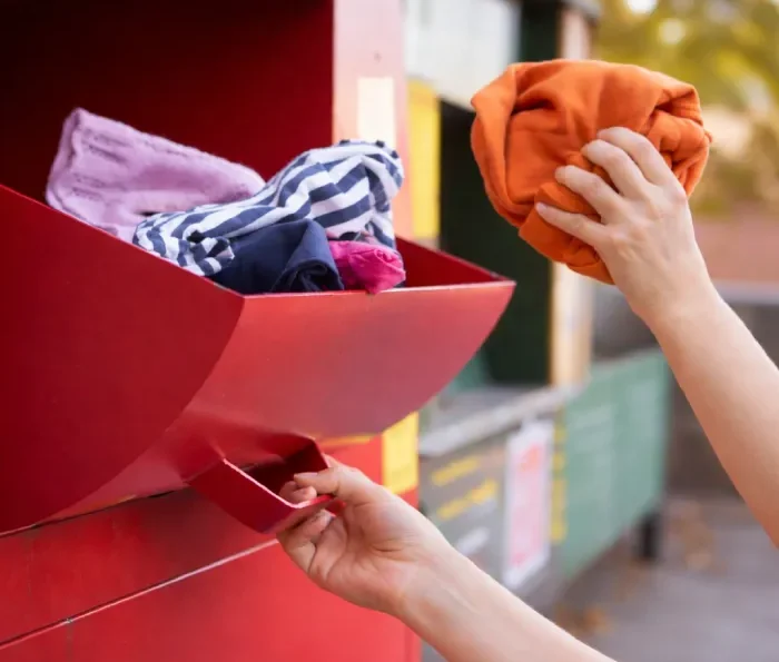 Persona depositando prendas en un punto de recogida de ropa usada